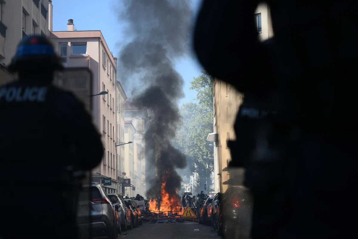 Estudantes em manifestação nas ruas da França cercados por agentes de segurança em trajes de confronto, em meio a clima de tensão e fumaça