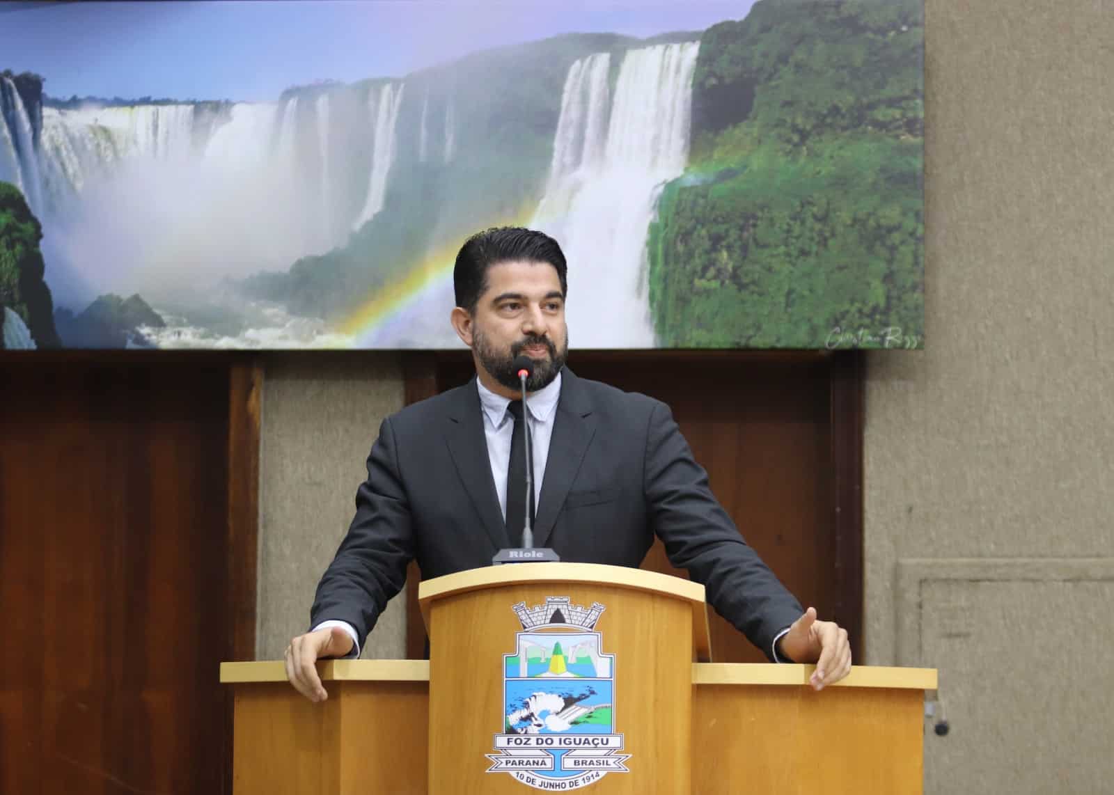 Vereador Adnan El Sayed em tribuna da Câmara Municipal de Foz do Iguaçu, com bandeiras do PT ao fundo, representando o contexto do pedido de cassação por apoio ao presidente Lula