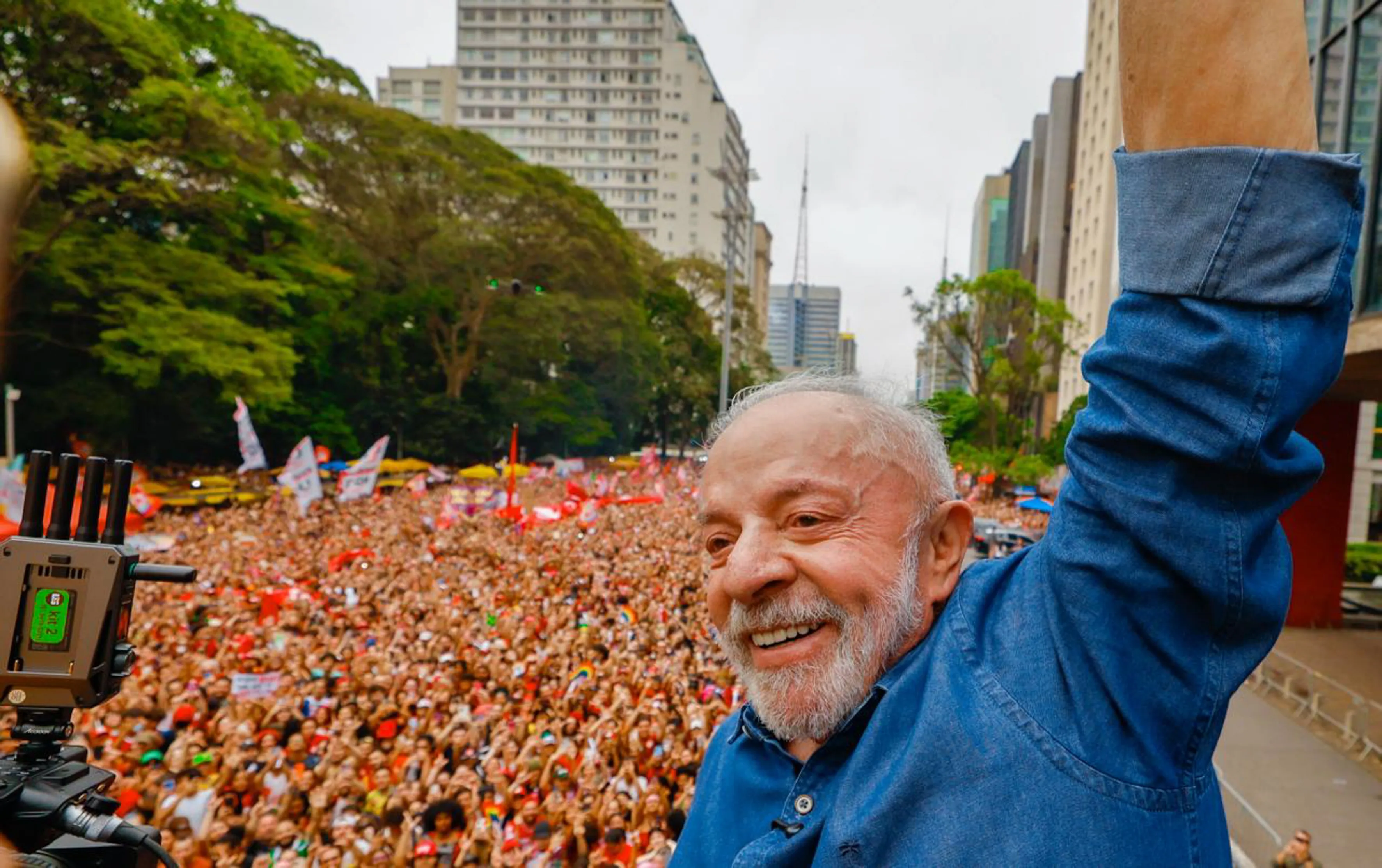 Ilustração representando disputa eleitoral no segundo turno entre Lula e Flávio Bolsonaro, com urnas e bandeiras do Brasil ao fundo