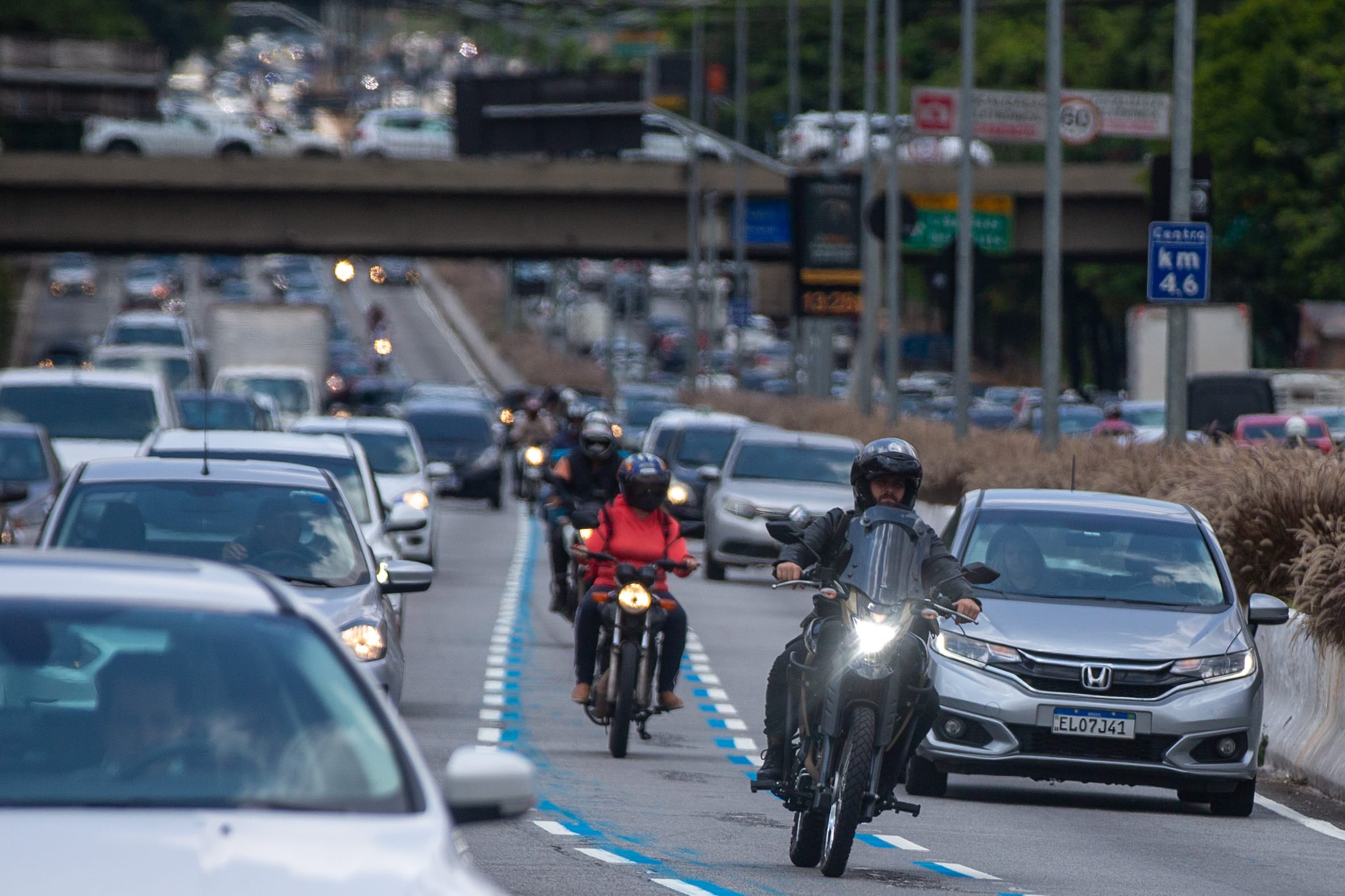 Motociclistas trafegando em faixa exclusiva sinalizada em azul em avenida de São Paulo, com trânsito intenso ao fundo