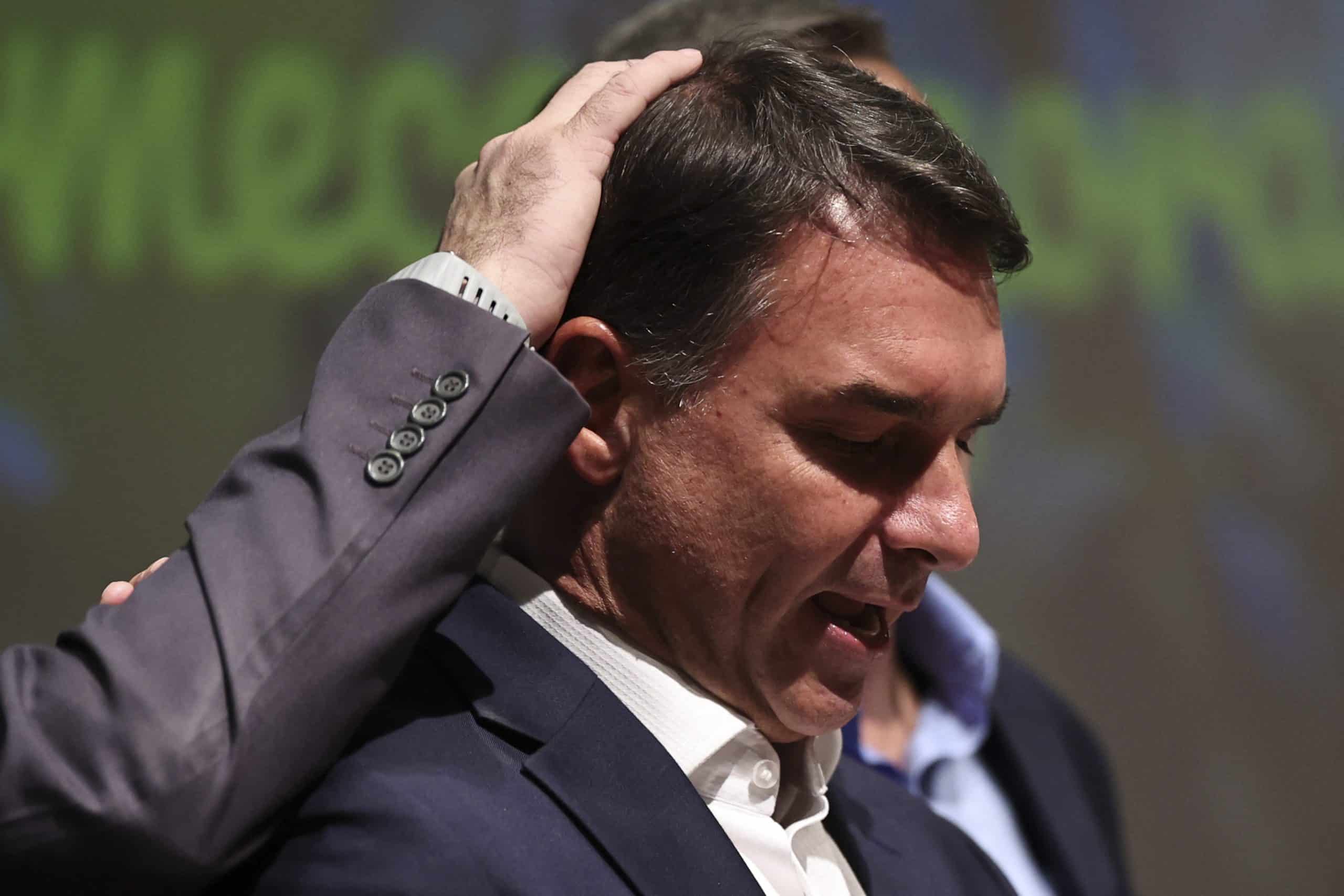 Flávio Bolsonaro durante entrevista ao Jornal Nacional da TV Globo, sentado em estúdio iluminado, em postura tensa diante dos apresentadores